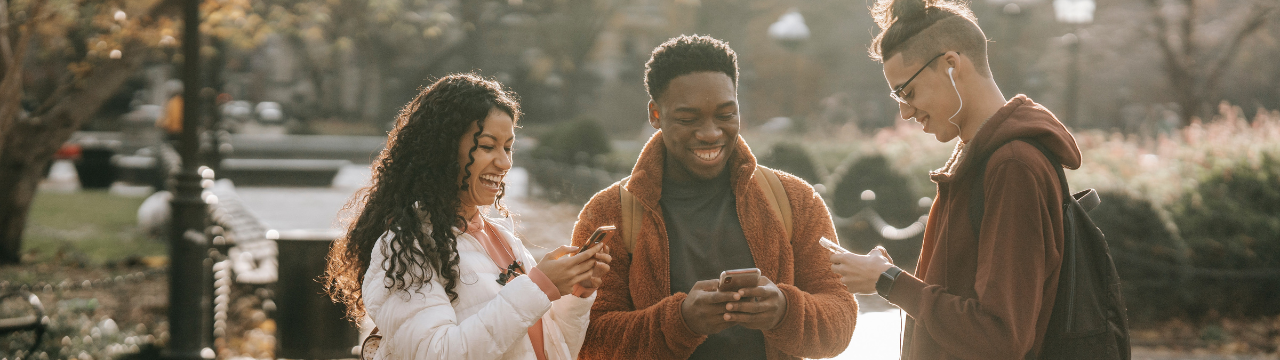 Three young adults smiling together while looking at their phones.